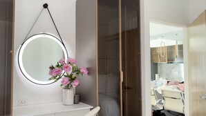 Une salle de bain avec un miroir rond, un vase de fleurs et un espace douche.