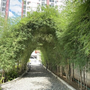 A pathway lined with bamboo trees, leading to a building with a red roof. - Delightful 2-bedroom apartment with AC in Lapu-Lapu (Lapu-Lapu)