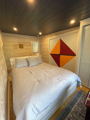 Une chambre à coucher avec un grand lit, des murs en bois, une porte ornée de motifs géométriques et une petite fenêtre.