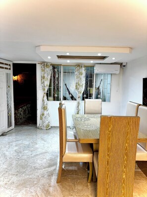 Un comedor con mesa y sillas, una ventana con cortinas e iluminación empotrada en el techo.