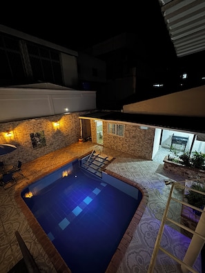 A swimming pool with a tiled deck, a small outdoor seating area, and a stone wall.