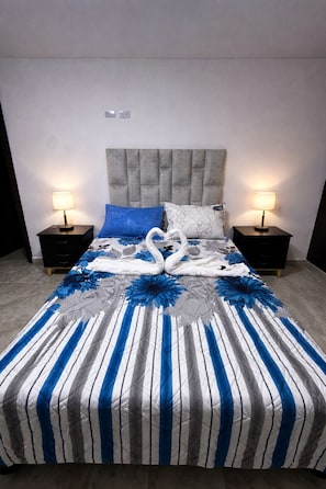 A bed with striped bedding, a grey headboard, and two bedside tables with lamps.