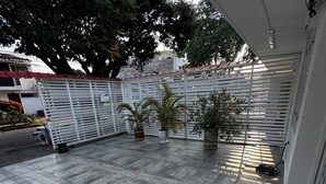 A covered outdoor area with tiled flooring, potted plants, and a white metal fence.
