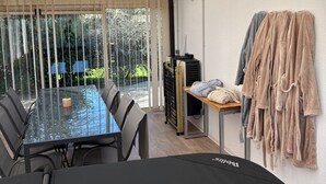 Una habitación moderna con una mesa de vidrio, sillas, una planta pequeña, un calentador y un perchero con toallas.