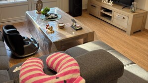 Una sala de estar con un sofá, un televisor, un sillón de masaje y una mesa de centro con objetos decorativos.