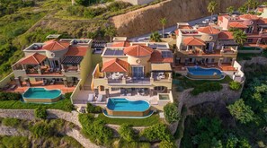 Un complejo turístico con varias edificaciones, piscinas al aire libre y un paisaje montañoso de fondo.