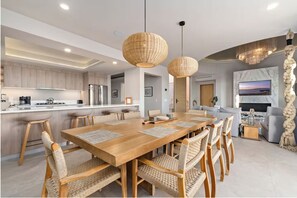 Una cocina moderna con una isla central, mesa de comedor de madera, sillas tejidas e iluminación colgante.