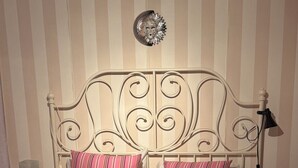 Ein Bett mit Metallgestell, zwei gestreifte Kissen, einer blumigen Tagesdecke und einem Wanddekor.