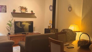 Ein Wohnzimmer mit Fernseher, Kamin, Tisch mit Lampe und einem Sessel.