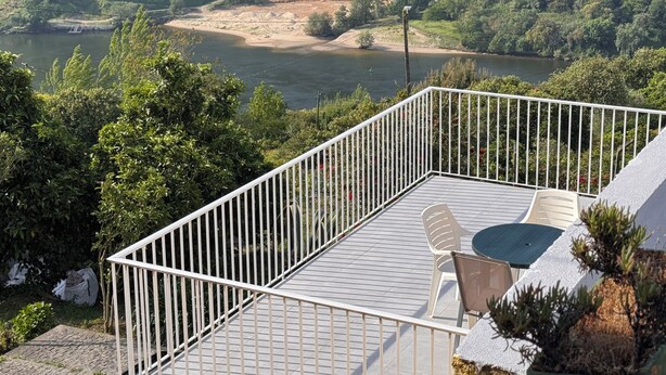 Eine Terrasse mit Blick auf einen Fluss und Treterrassierungen, ein Tisch mit Stühlen und ein kleines Gebäude im Hintergrund.