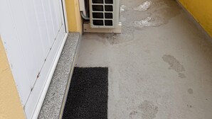 Ein Balkon mit gelber Wand, einer weißen Klimaanlage und einer schwarzen Fußmatte.