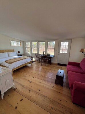 A room with a bed, a desk, a chair, a red sofa, and large windows. - BRAND NEW LISTING!!! Rustic cabin at historic orchard & cidery. Pet-Friendly! (New Salem)