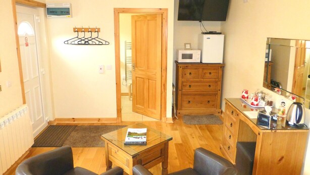 Una stanza piccola e ben illuminata con una porta in legno, una televisione a parete, un forno a microonde, un mobiletto e un tavolino in vetro con due sedie.