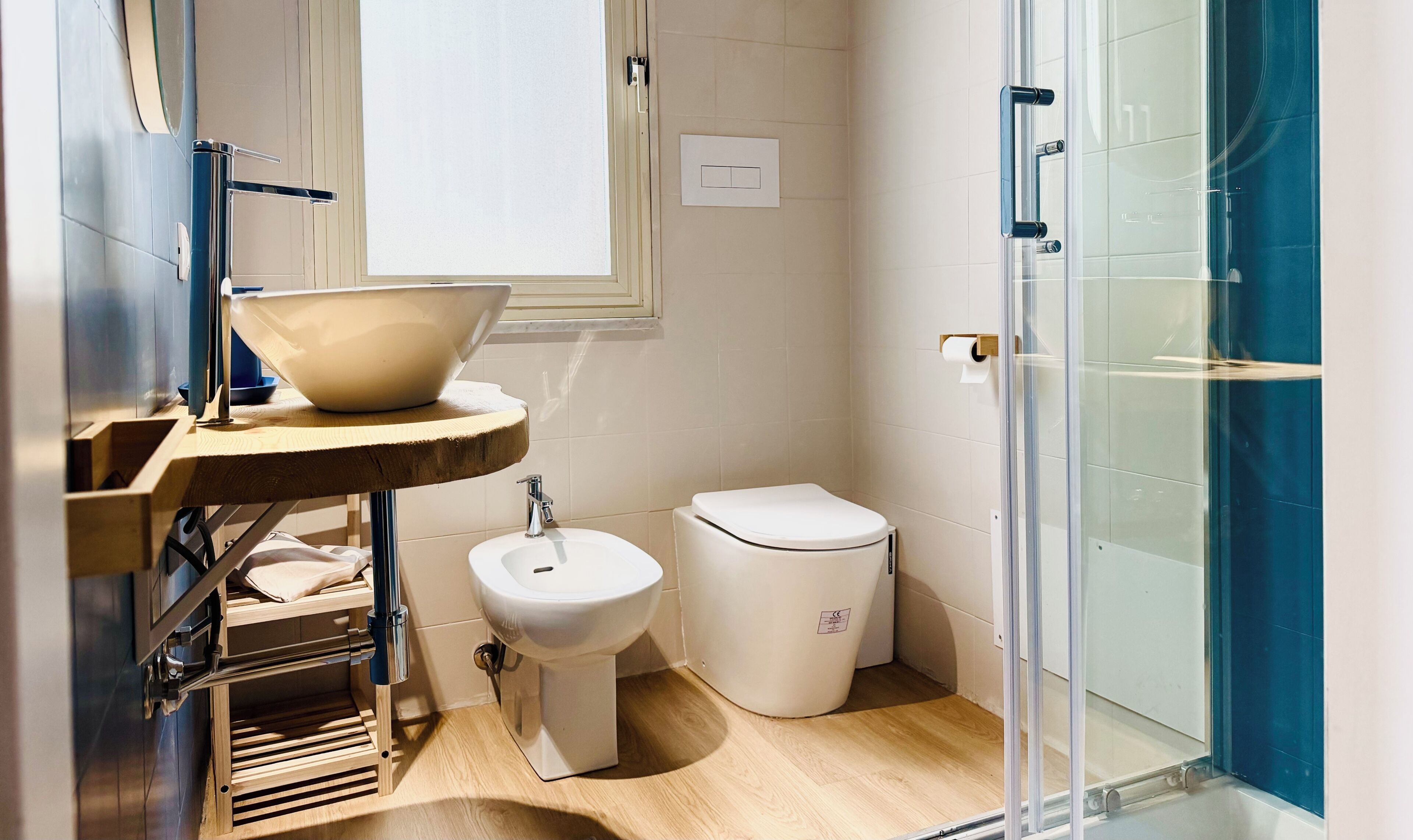 Ein Badezimmer mit einem Holz-Waschtisch, einem weißen Waschbecken, einer Toilette und einer Duschkabine aus Glas.