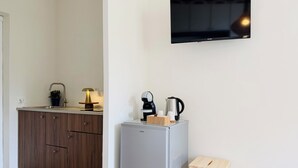 Et køkken med vask, skabe, et køleskab, en lille træskammel og et fjernsyn monteret på væggen.