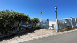 En lukket indgang med et skilt for KefaHelion Residence, en belagt sti og en klar blå himmel.