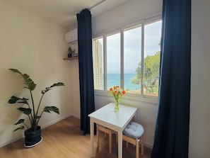 A room with a white table, a chair, a potted plant, a window with curtains, and a view of the sea. - CEFALUCE - Corner of Paradise in Cefalù (Cefalù)