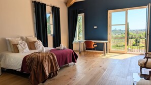 A bedroom with a bed, a desk, and a chair, a balcony with a view, and a window with curtains. - Wine estate | 20m pool and cinema (Pézenas)