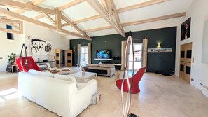 A spacious living room with a white sofa, red chairs, a flat-screen TV, and a large painting on the wall. - Wine estate | 20m pool and cinema (Pézenas)