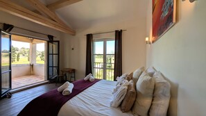 Ein Schlafzimmer mit einem großen Bett, Blick ins Freie durch eine Schiebetür und einem Gemälde an der Wand.