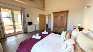 Ein Hotelzimmer mit einem großen Bett, einem Holzschrank, einem Schreibtisch mit Computer und Blick durch eine Glastür.