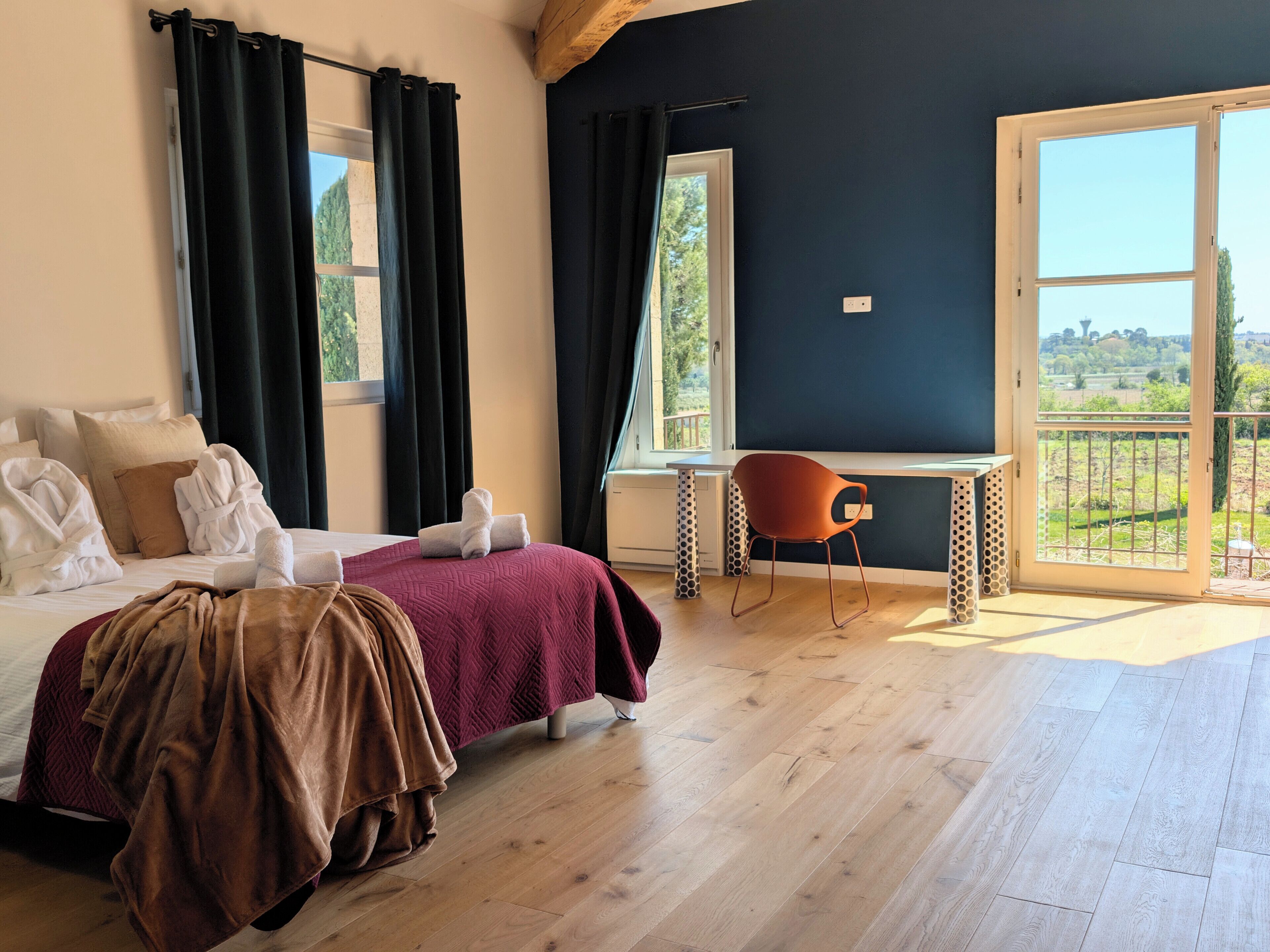 A bedroom with a bed, a desk, and a view of the outdoors.
