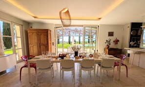 A dining area with a table set for six, large windows, and a view of the outdoors. - Wine estate | 20m pool and cinema (Pézenas)
