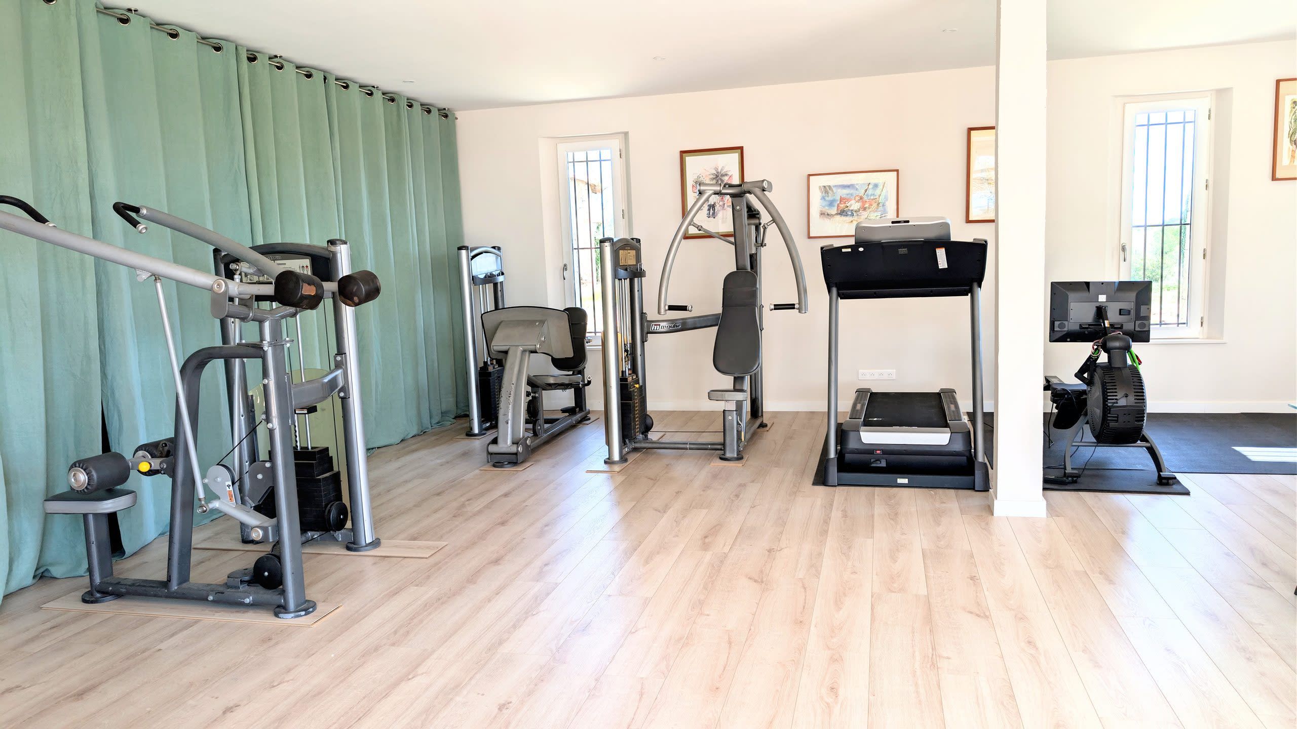 Une salle de sport équipée de divers appareils d’exercice, notamment un tapis de course, des appareils de musculation et un rameur.