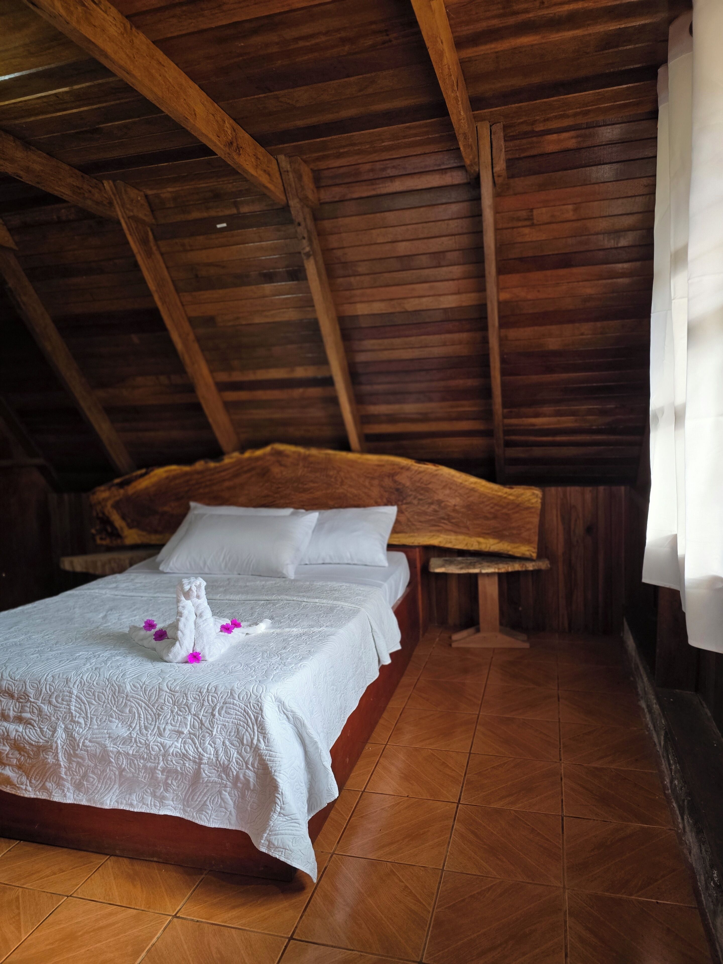 A room with a wooden ceiling, a bed with white bedding, and a wooden headboard.