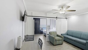 A modern hotel room with a bed, a blue sofa, a small armchair, a ceiling fan, and a view through a door. - Daytona Bike Week at Mavrick Resort on beautiful Ormond Beach! (Ormond Beach)
