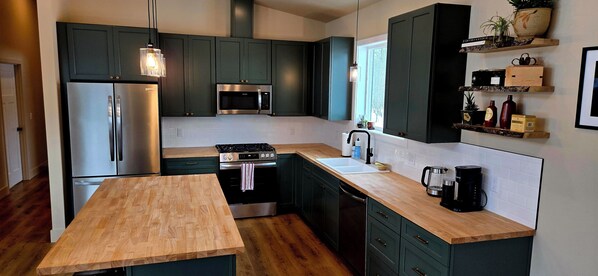 A modern kitchen with dark cabinets, stainless steel appliances, a wooden table, and a coffee maker.