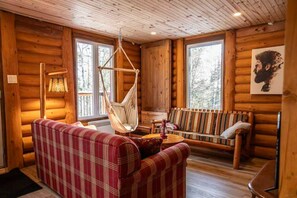 A log cabin interior with a plaid sofa, a hammock, and a wooden floor.