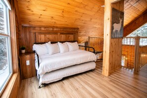 A wooden cabin bedroom with a bed, a nightstand, a window, and a door.