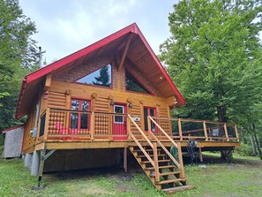 A two-story log cabin with a red roof, a balcony, and a staircase leading to the upper floor. - La Sainte-Paix log cabin in St-Fabien de Panet (Saint-Fabien-de-Panet)