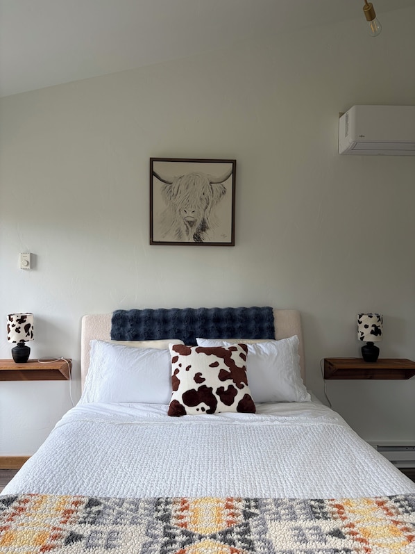 Ein Schlafzimmer mit einem Bett, einem Kissen mit Kuhmuster, einem gerahmten Kunstwerk, Nachttischen und einer Lampe.