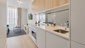 Een moderne keuken met een groot eiland, roestvrijstalen apparatuur en uitzicht op de woonkamer.