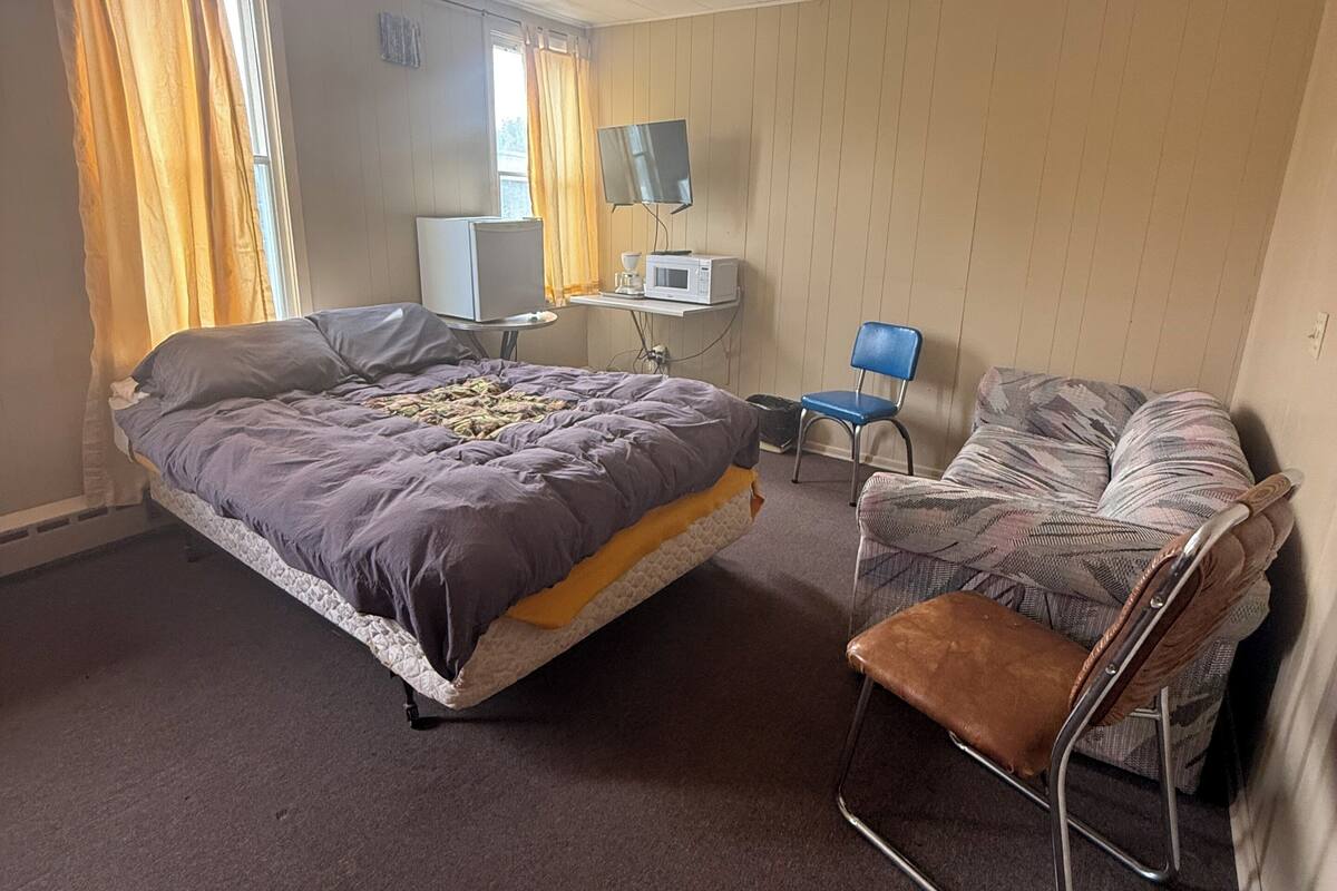 A hotel room with a bed, a small table with a microwave, a chair, and a TV.