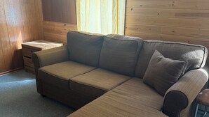 Een bruine modulaire bank met een voetenbankje, een klein houten nachtkastje en een raam met gordijnen.