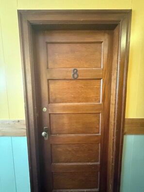 A wooden door with a metal number plate and a door handle. - Coal Branch Hotel (Robb)