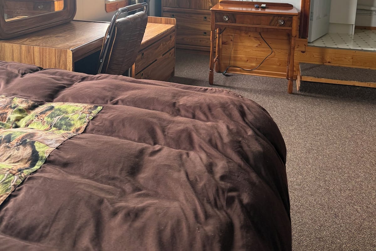 A bedroom with a bed, a desk, a chair, a wardrobe, and a television.