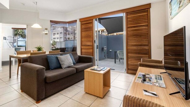 A modern living room with a sofa, coffee table, and TV, featuring a sliding glass door to a balcony. - 2 Bedroom Courtyard Poolside (Kings Beach)