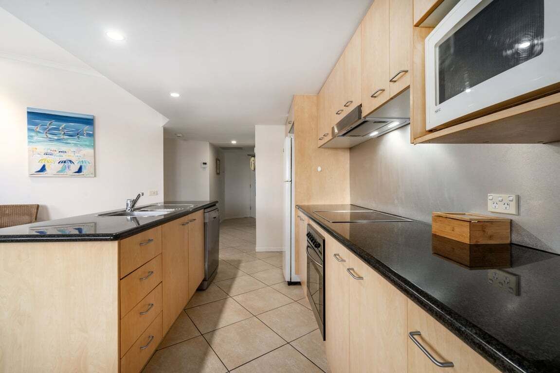 A modern kitchen with wooden cabinets, a black countertop, and a microwave.