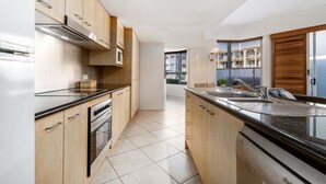 A modern kitchen with wooden cabinets, a built-in oven, and a large island with a sink. - 2 Bedroom Courtyard Poolside (Kings Beach)