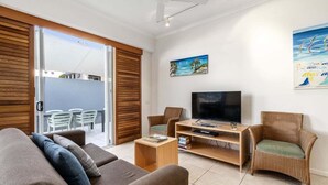 A modern living room with a sofa, chairs, a TV, and a sliding glass door leading to an outdoor area. - 2 Bedroom Courtyard Poolside (Kings Beach)