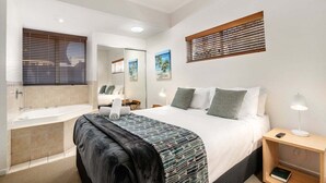 A hotel room with a bed, bedside table, lamp, and a bathroom with a bathtub and sink. - 2 Bedroom Courtyard Poolside (Kings Beach)