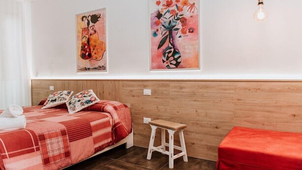 Une pièce comprenant un lit, un petit tabouret et deux tableaux accrochés au mur.
