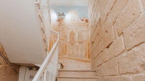 Un escalier orné d’une fresque murale, avec une rampe blanche et un luminaire.