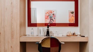Un bureau en bois avec un miroir, une chaise et divers objets, notamment une bouilloire, une tasse et une petite plante.