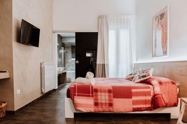 Un dormitorio con cama, televisión, baño y un cuadro en la pared.