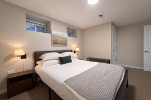 Ein Schlafzimmer mit einem Bett, zwei Nachttischlampen, einem Nachttisch, einem kleinen Tisch, einer Tür und einem Fenster.